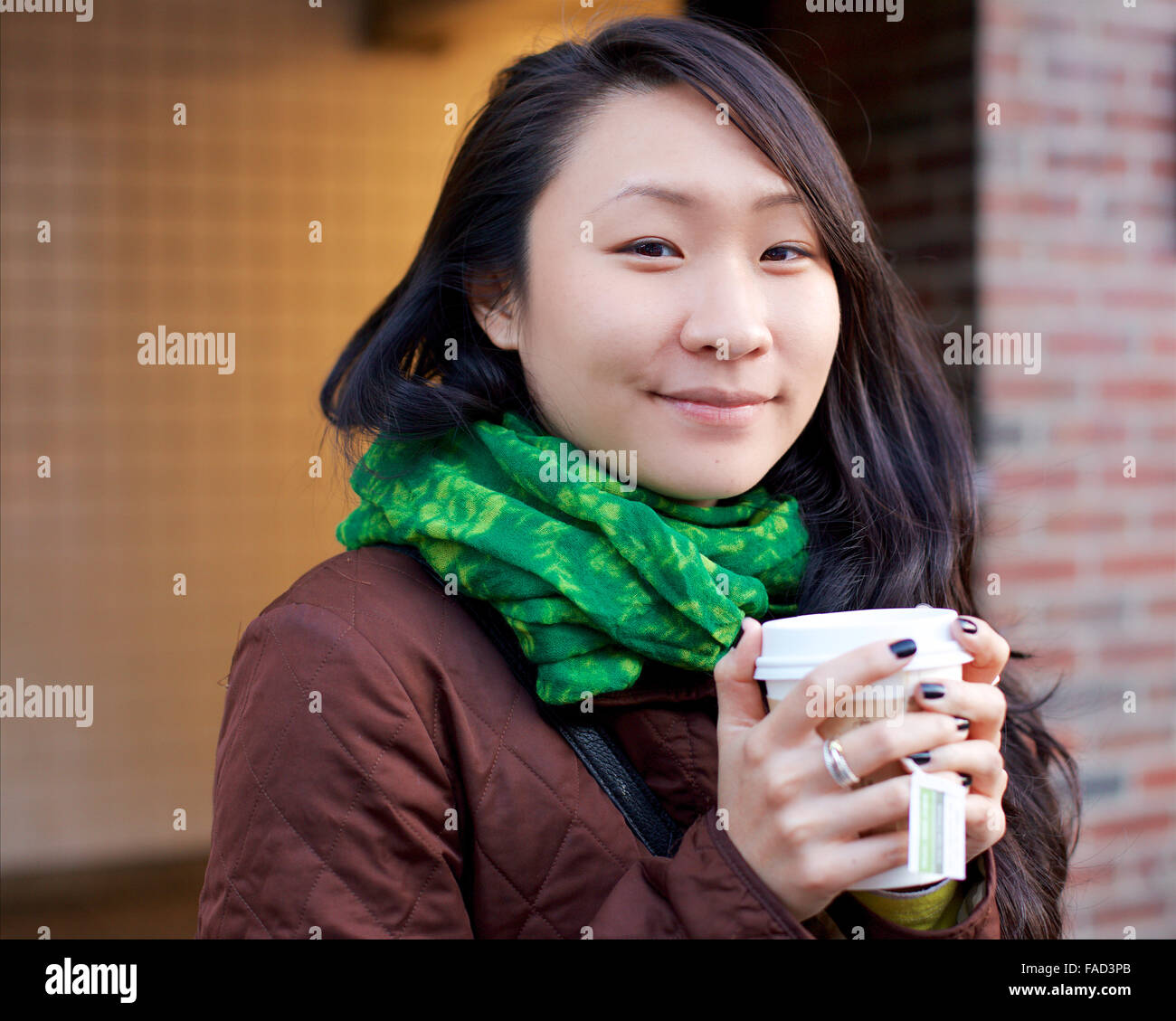 Young Asian woman sourit à la caméra alors que ses mains réchauffement avec du thé dans une tasse de papier dans l'hiver rues de Manhattan. Banque D'Images