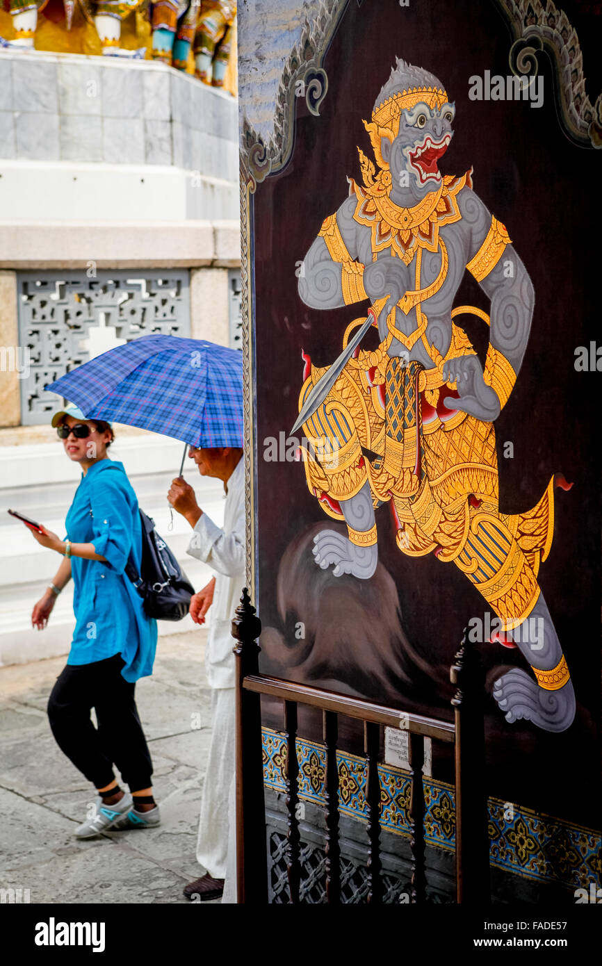 Personnes passant près de la porte murale décorée avec la peinture traditionnelle de démon au complexe de palais grandiose de Bangkok. Banque D'Images