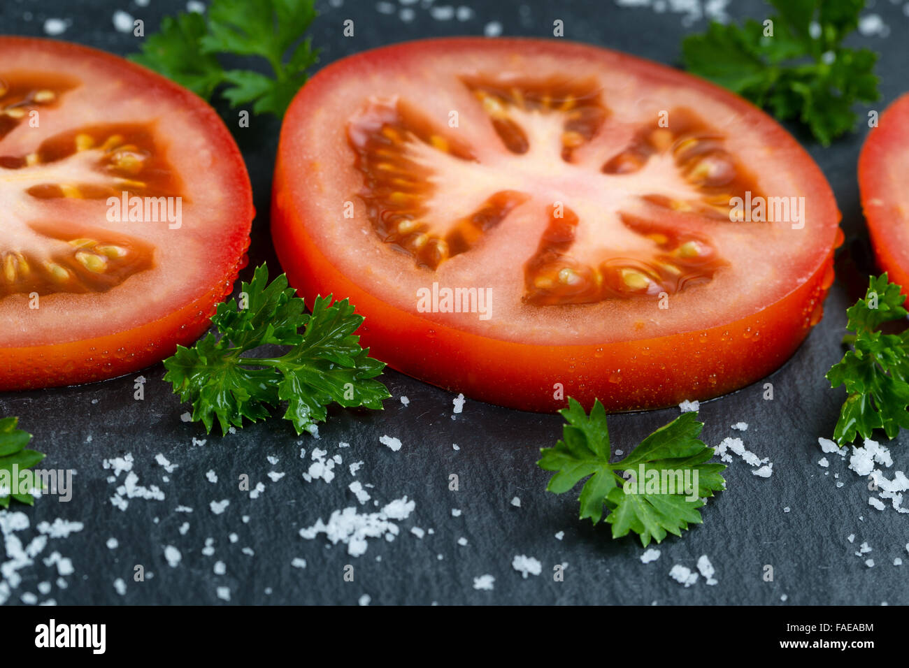 Close up vue avant de juicy tranches de tomate mûre, de persil et de sel de mer naturel flocons sur ardoise en pierre. Banque D'Images