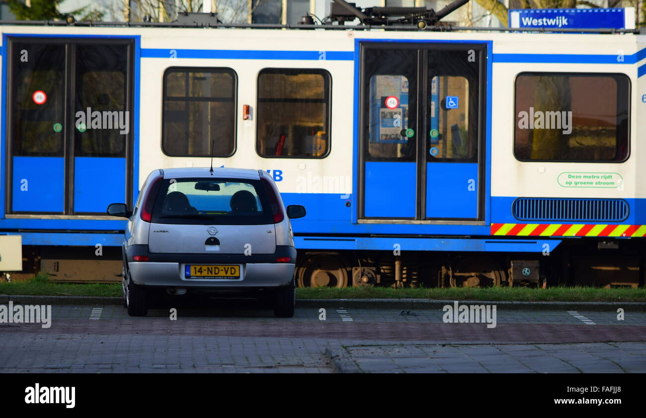 Un livre blanc et bleu de tramway d'Amsterdam en passant par un bleu clair voiture garée dans un lot. Banque D'Images