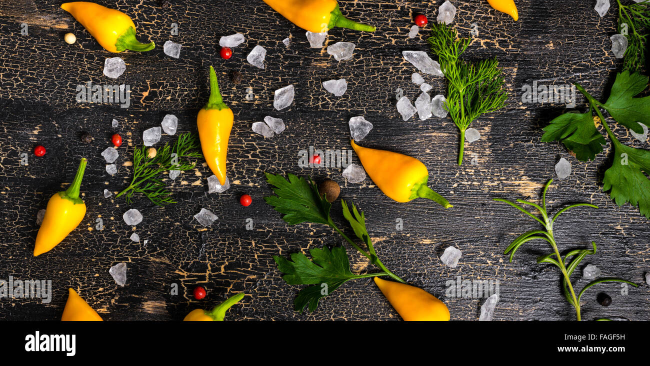 Vue de dessus de jaune Hot Chili Peppers, sel de mer, de verdure sur fond noir des fissures, panorama Banque D'Images