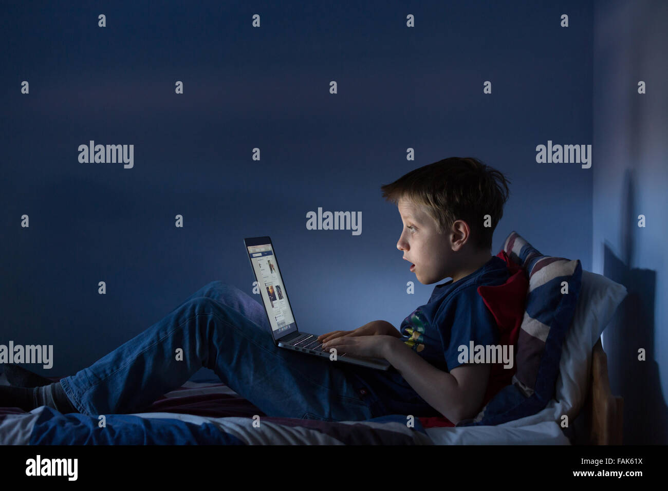 Un garçon assis jusqu'à la fin de sa chambre à la recherche sur l'internet choqué par ce qu'il voit Banque D'Images