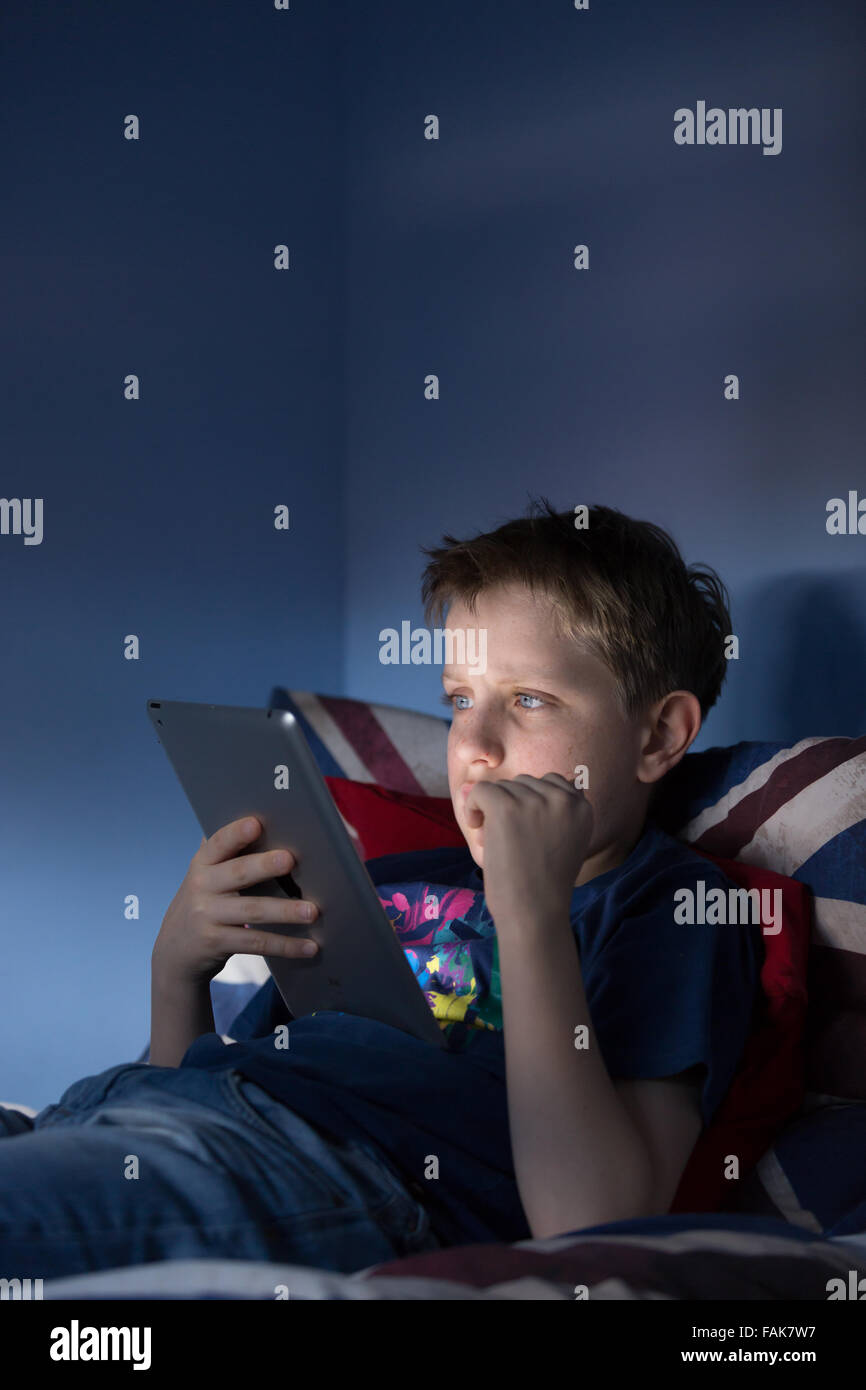 Un garçon assis jusqu'à la fin de sa chambre à la recherche sur l'internet choqué par ce qu'il voit Banque D'Images