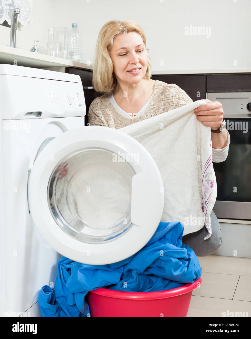 Vieille Femme faisant la blanchisserie avec lave linge la maison