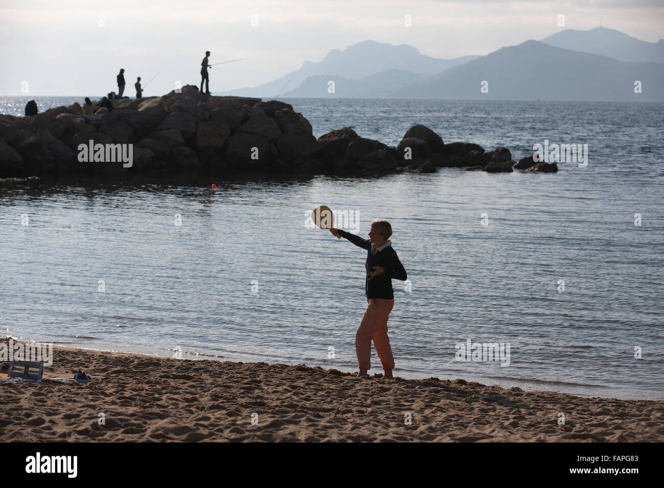 Les amateurs de soleil d'hiver bénéficiant d'une journée ensoleillée sur la Rviera beach, boulevard du Midi Jean Hibert, Cannes, Côte d'Azur, France Banque D'Images