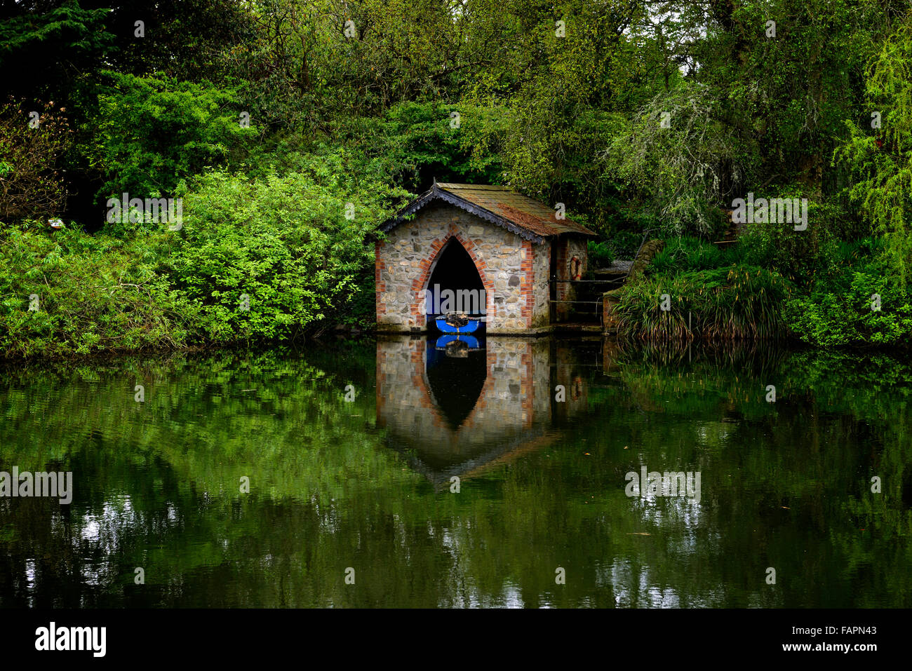 Lac étang bleu bateau hangar hangar en brique immobilier reflètent la réflexion encore tranquille jardin floral fonction RM Banque D'Images