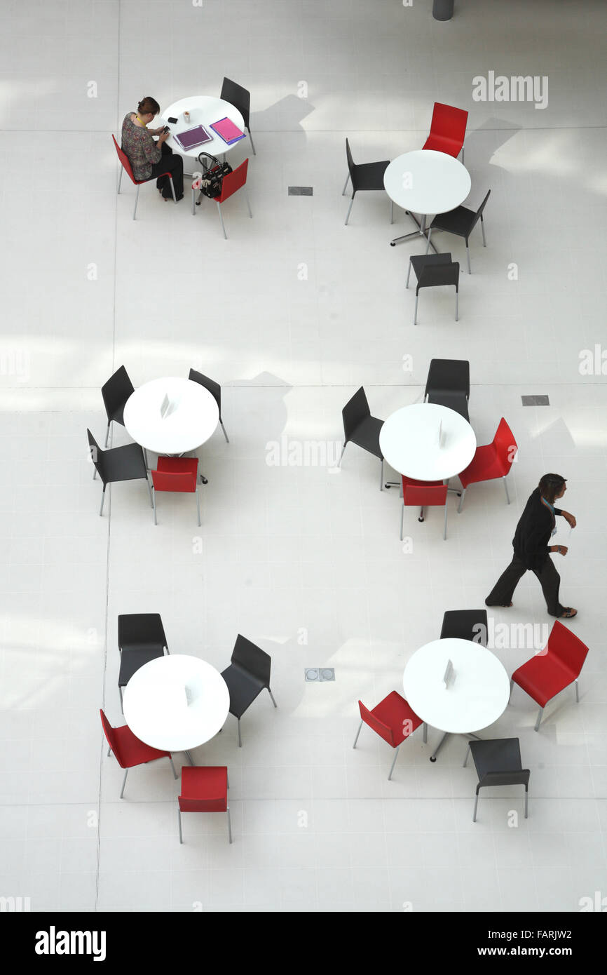 Vue de haut niveau des tables de cantine dans un collège moderne bâtiment. Montre une personne assise et de travail, une personne qui marche Banque D'Images