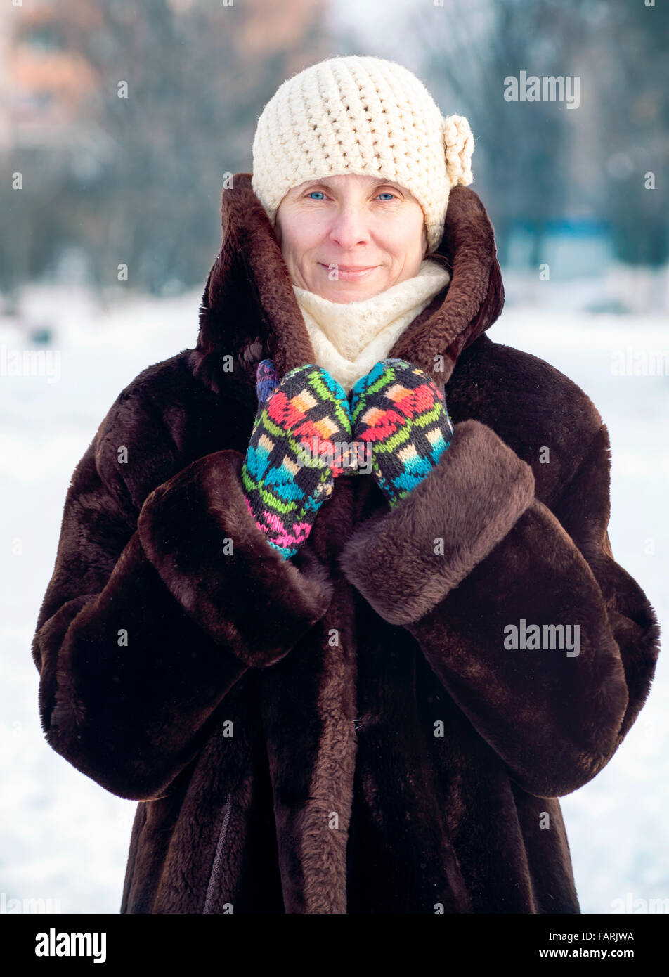 Un hiver portrait of a smiling senior femme portant un chapeau de laine, une écharpe et des gants de couleur, avec un fond de neige Banque D'Images