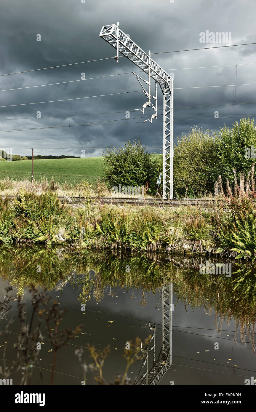 Traverse haute pour lignes de train électrifié UK en campagne avec canal en premier plan Banque D'Images