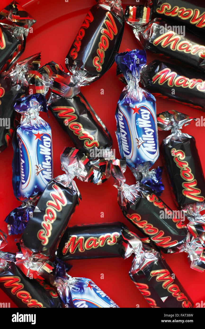 Voie lactée et Mars fun size bars à gauche dans le fond d'un remous de chocolats. Banque D'Images