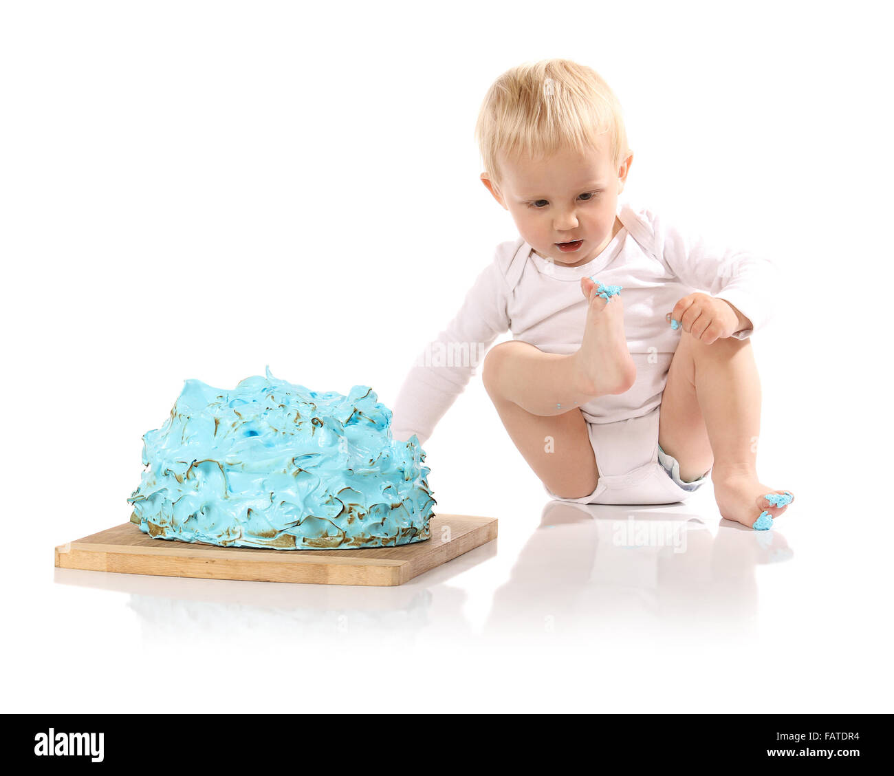 Un petit garçon âgé d'un an brisant une anniversaire glacé bleu gâteau sur une planche de bois. L'image est isolé sur un fond blanc. Banque D'Images