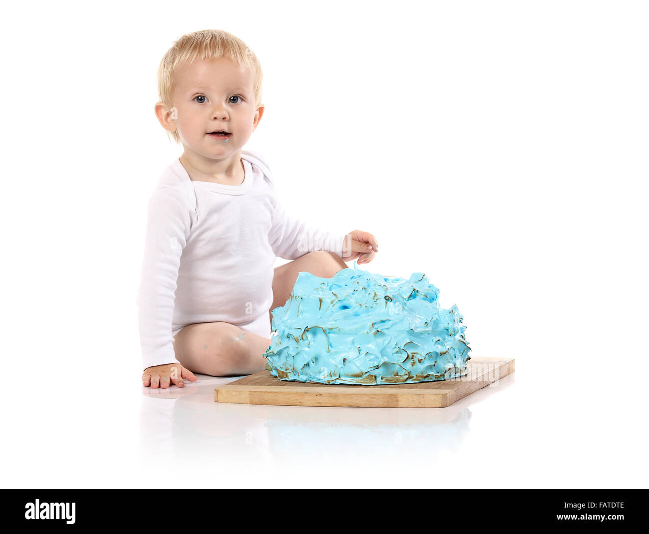 Un petit garçon âgé d'un an brisant une anniversaire glacé bleu gâteau sur une planche de bois. L'image est isolé sur un fond blanc. Banque D'Images