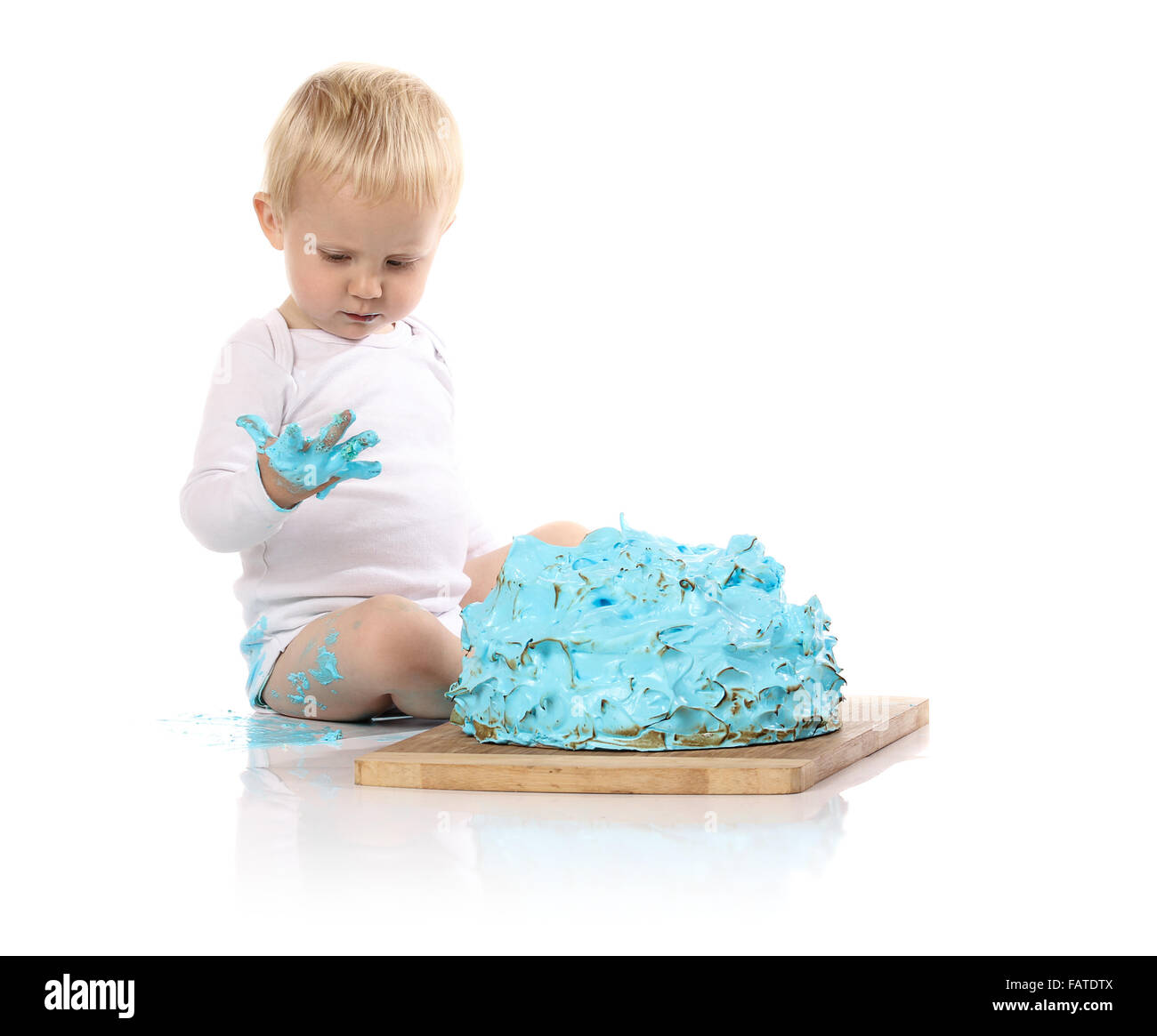 Un petit garçon âgé d'un an brisant une anniversaire glacé bleu gâteau sur une planche de bois. L'image est isolé sur un fond blanc. Banque D'Images