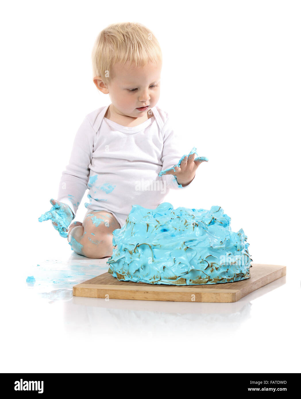 Un petit garçon âgé d'un an brisant une anniversaire glacé bleu gâteau sur une planche de bois. L'image est isolé sur un fond blanc. Banque D'Images