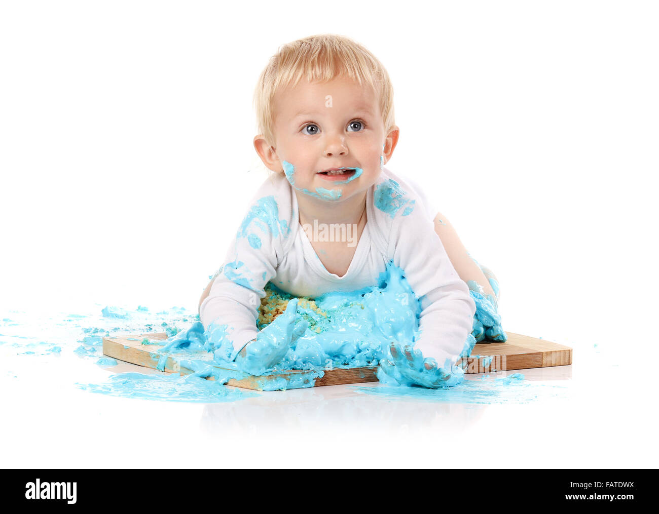 Un petit garçon âgé d'un an brisant une anniversaire glacé bleu gâteau sur une planche de bois. L'image est isolé sur un fond blanc. Banque D'Images