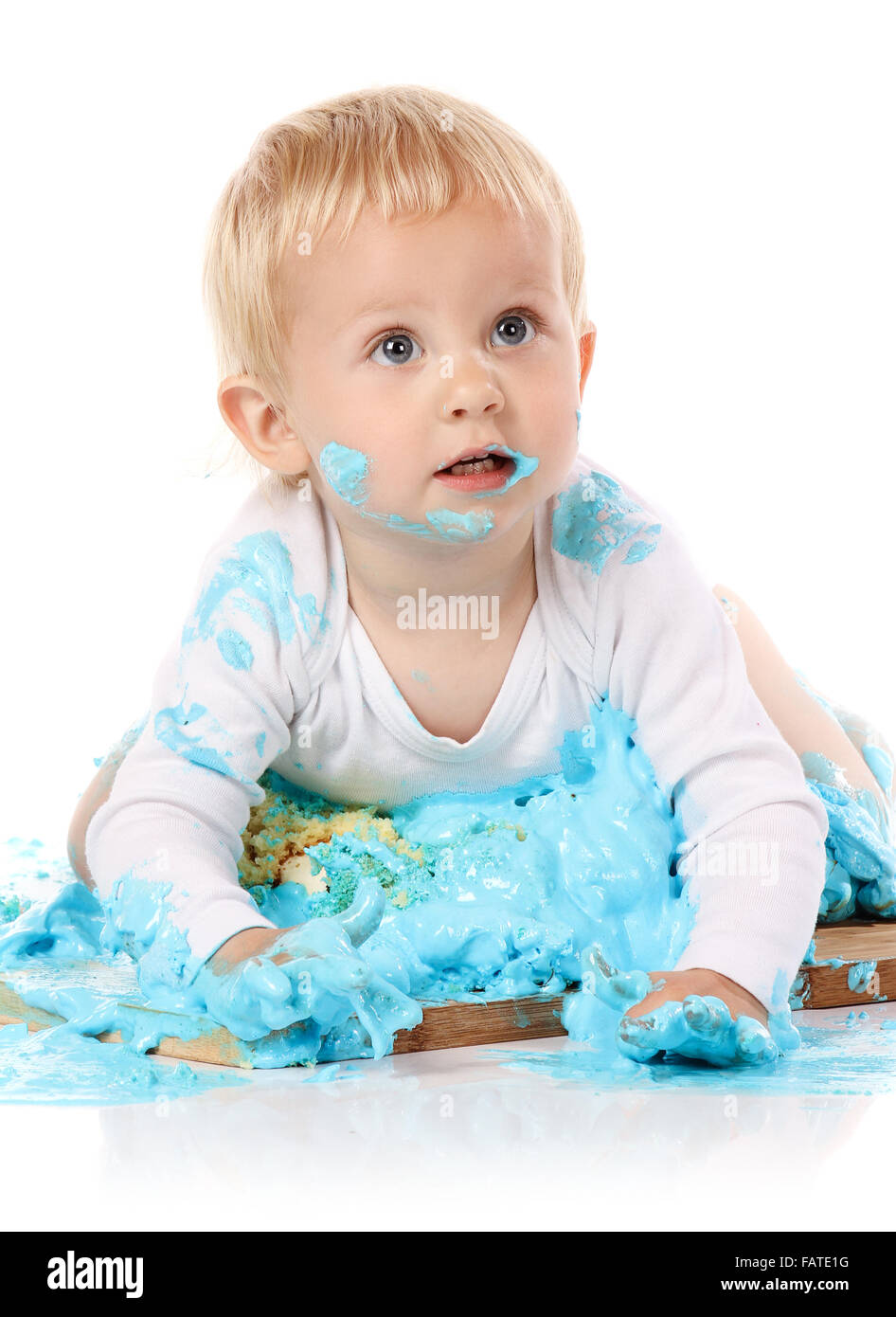 Un petit garçon âgé d'un an brisant une anniversaire glacé bleu gâteau sur une planche de bois. L'image est isolé sur un fond blanc. Banque D'Images