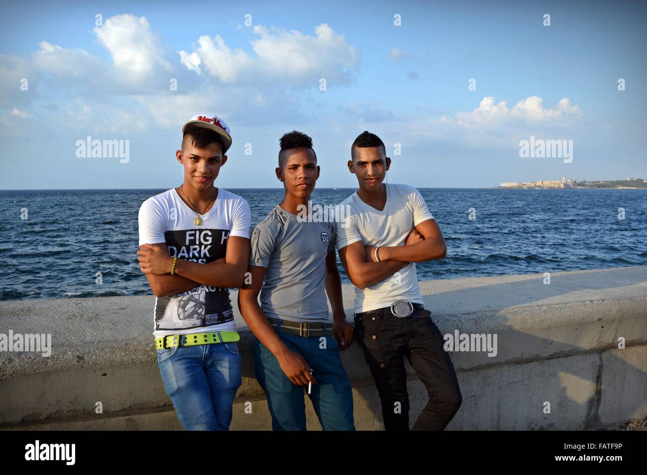 Trois jeunes hommes à la mode cubaine se penchant sur la digue à fumer une cigarette sur le Malecon esplanade côtière à La Havane, Cuba Banque D'Images