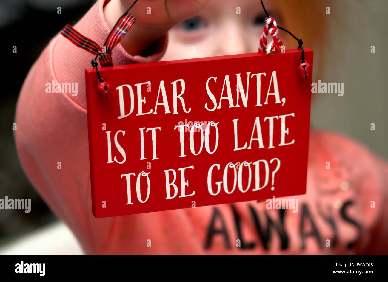 Une fillette de 3 ans avec un visage triste tenant une plaque avec le message Cher Père Noël est-il trop tard pour être bon ? Banque D'Images