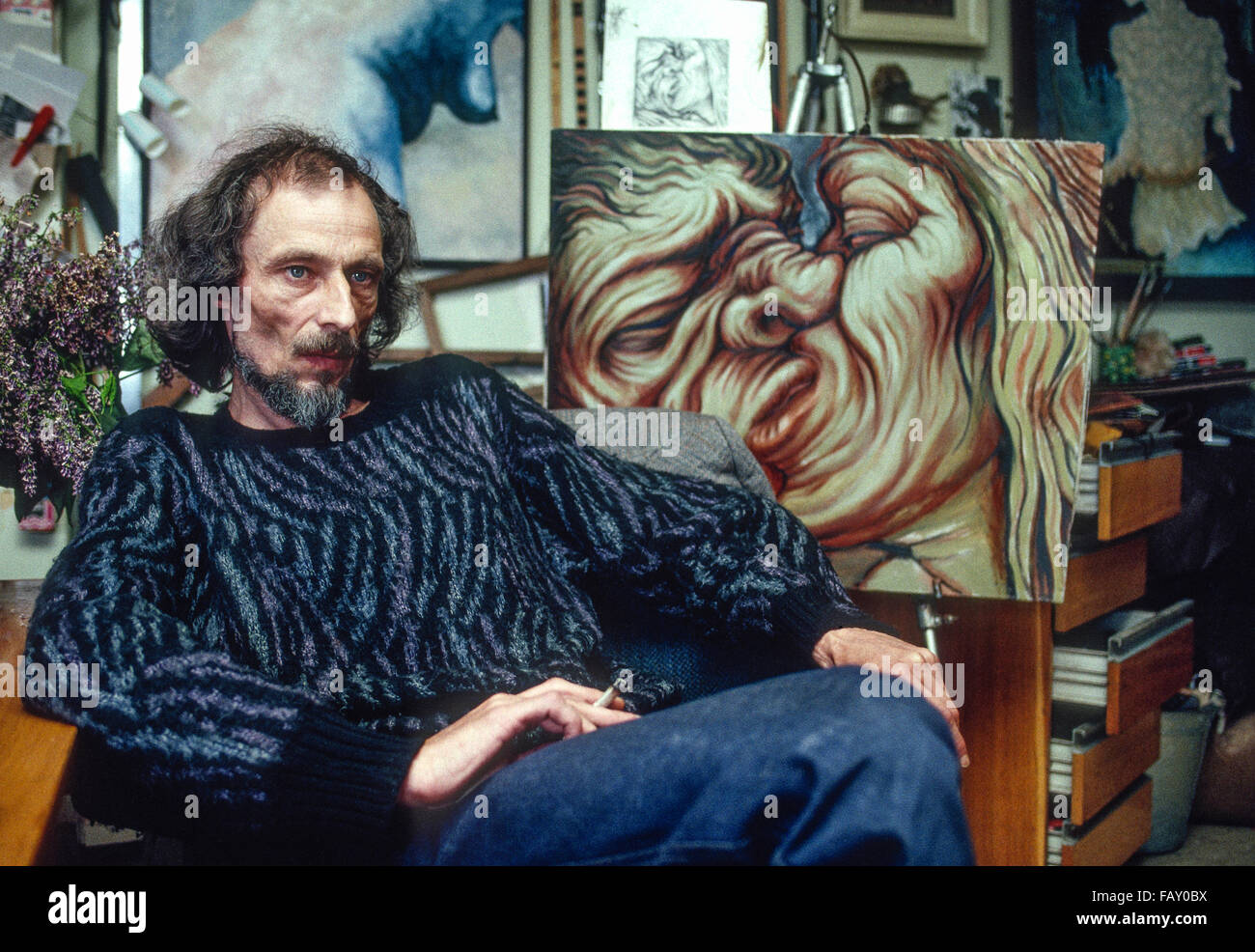 Peintre contemporain de Sibérie hommes assis sur une chaise dans son studio de fumer une cigarette à côté de l'un de ses tableaux d'un couple Banque D'Images