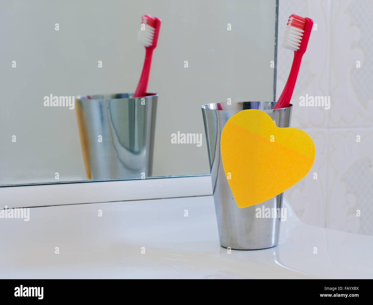 Mug en brosse à dents dans la salle de bains avec coeur postit. Rappel. Focus différentiel. Banque D'Images