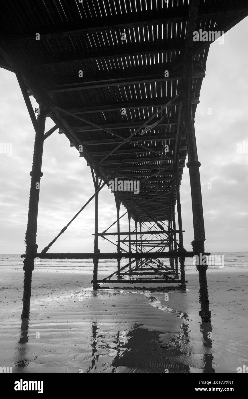 Sous la structure de l'ancienne jetée Bognor Regis. Les marées le ciel est gris, un rhume moody tourné en monochrome. Banque D'Images
