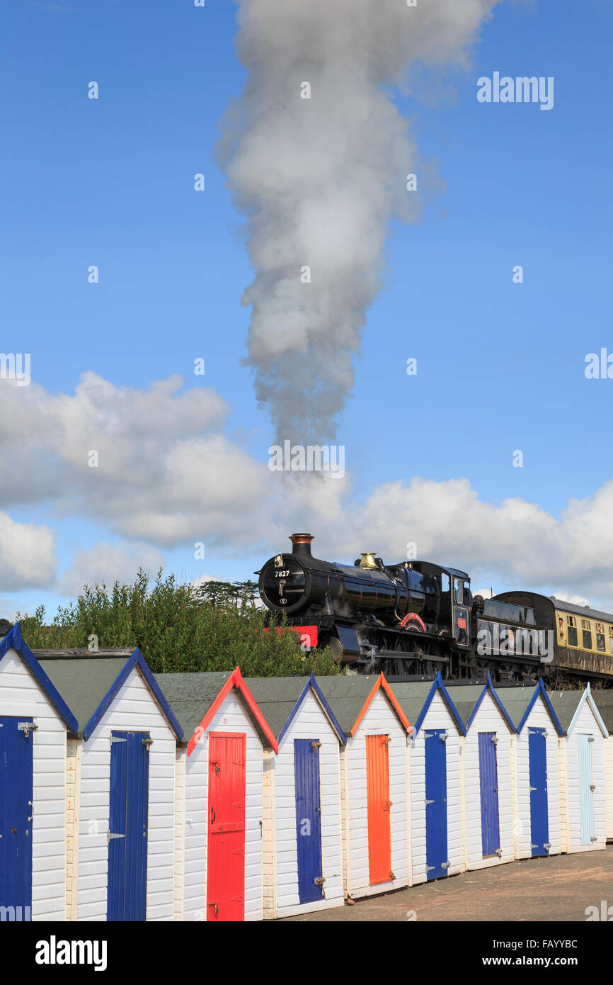 7827 Lydham Manor tire un train passé les cabanes de plage de Goodrington Sands, Paignton, Devon, de manière partiellement nuageux à la fin de journée d'été Banque D'Images