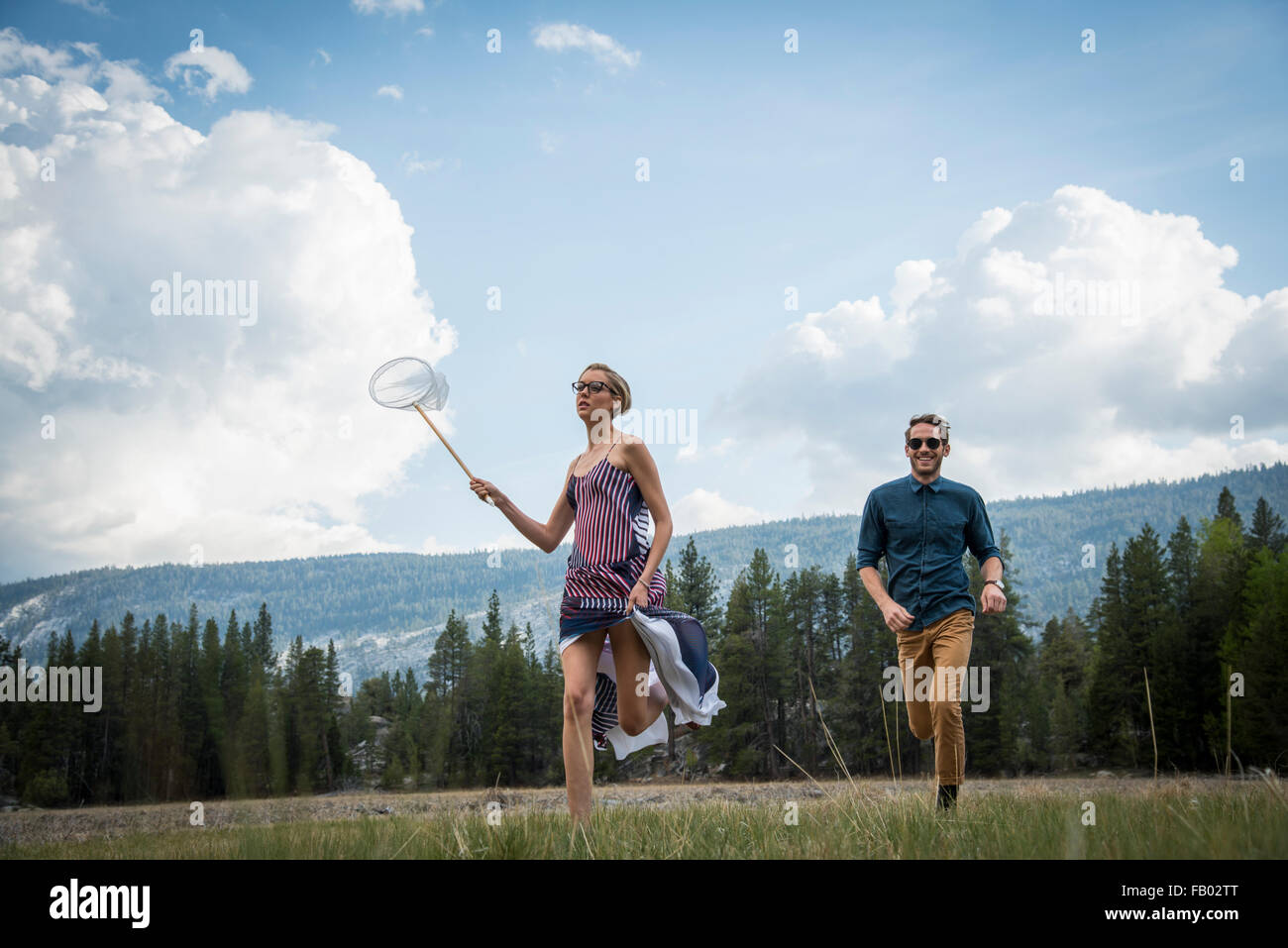 Jeune couple qui traverse une prairie attraper les papillons. Banque D'Images