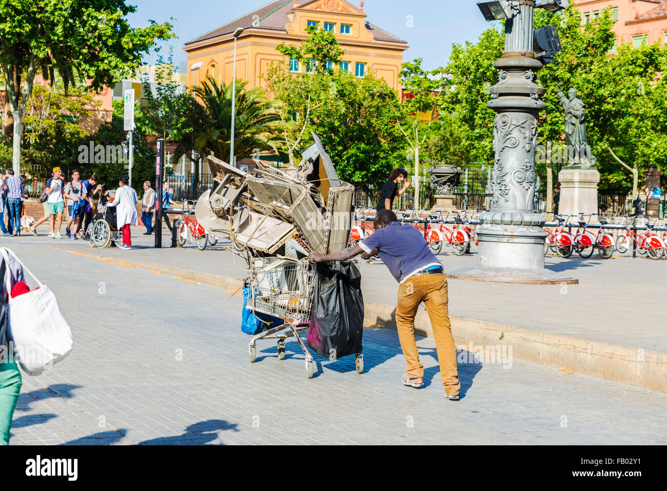 Homme noir en poussant un chariot plein de ferraille entouré par les touristes à Barcelone, Catalogne, Espagne Banque D'Images