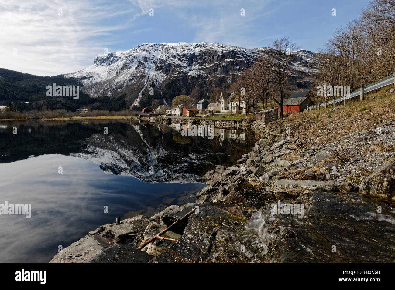 Réflexion d'un petit village sur les rives du lac de Granvinsvatnet flanquée d'une montagne surmontée d'un peu de neige. Banque D'Images