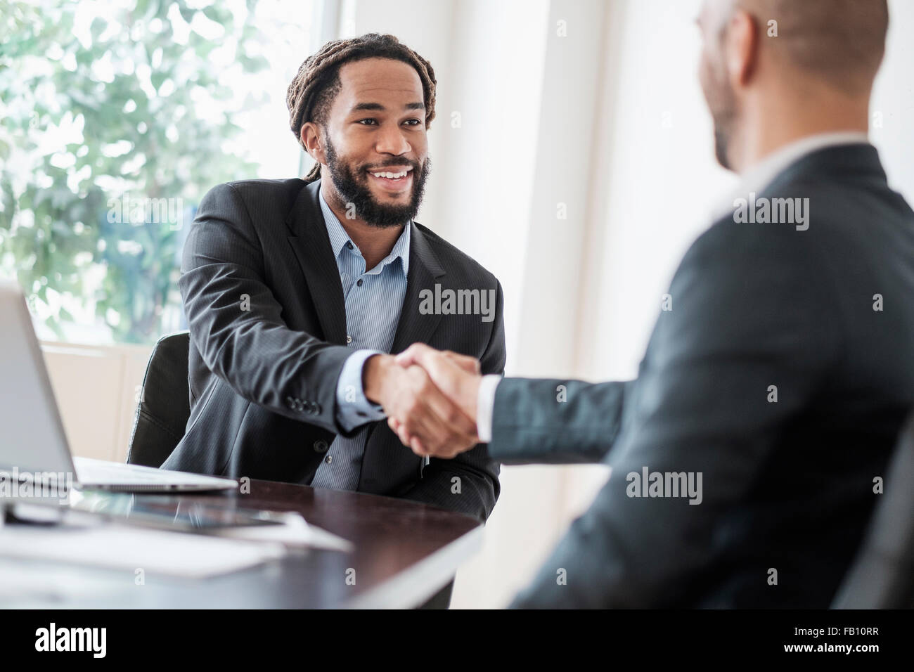 Smiling businessmen shaking hands in office Banque D'Images
