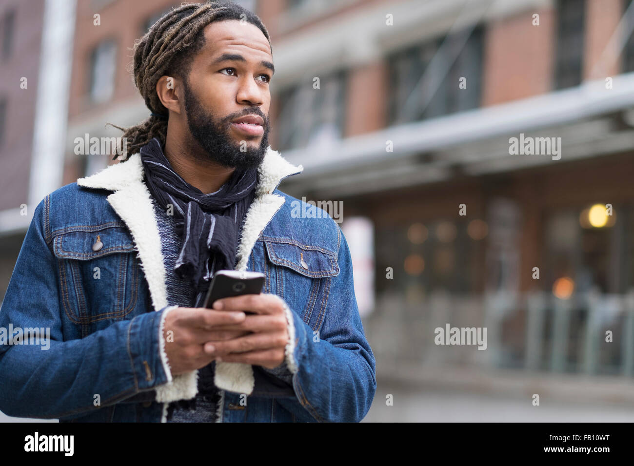 Homme sérieux avec des dreadlocks holding smart phone in street Banque D'Images