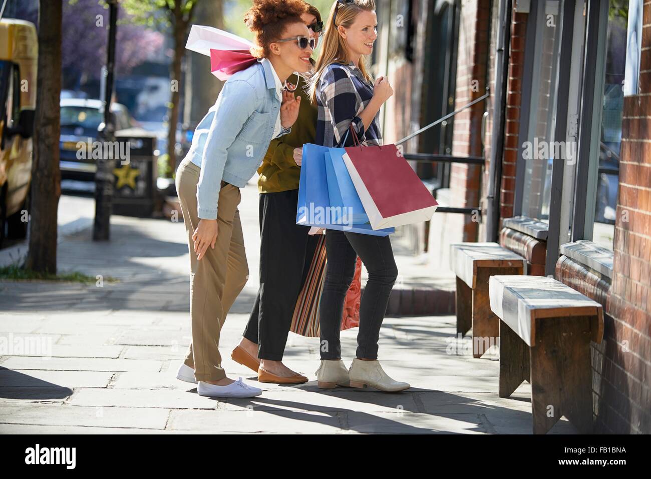 Vue latérale de la femme holding shopping bags standing in street à la recherche de vitrine Banque D'Images