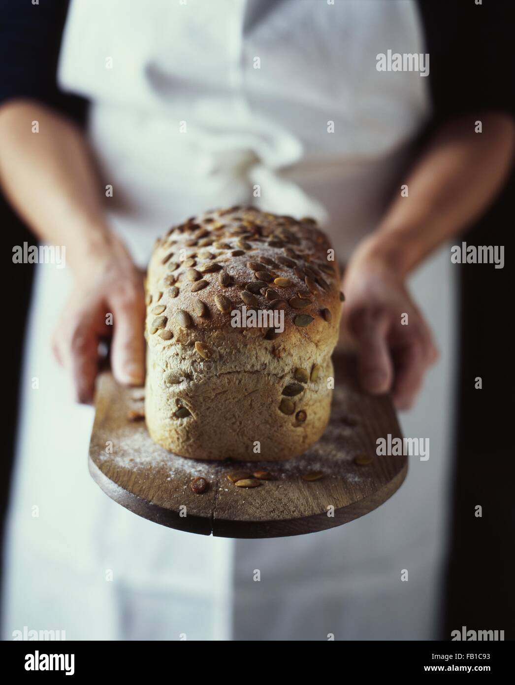Mains de femme baker holding fresh du four pain bio ensemencée sur breadboard Banque D'Images