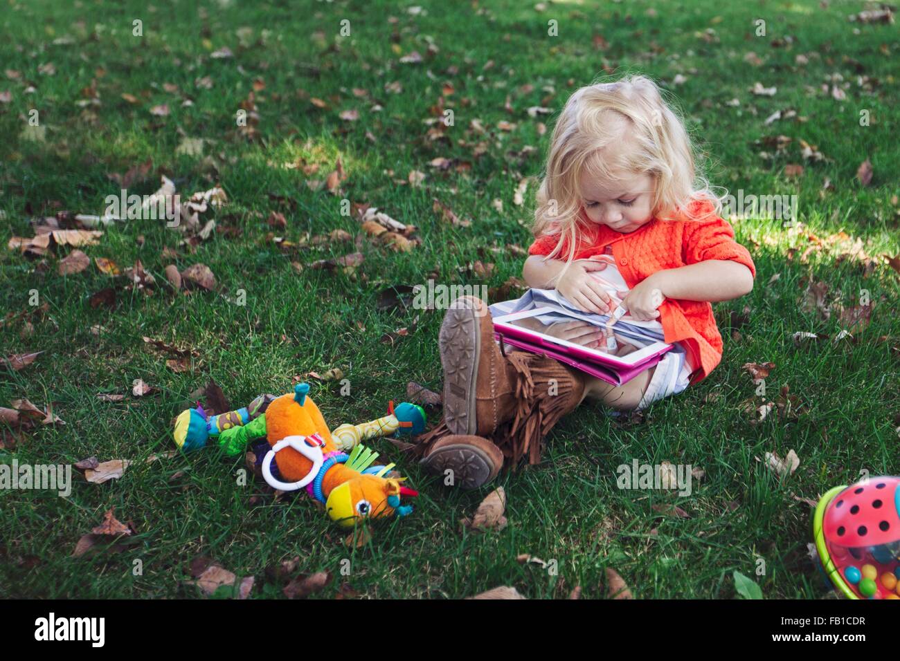 Fille assise sur l'herbe avec des jouets à bas using digital tablet Banque D'Images