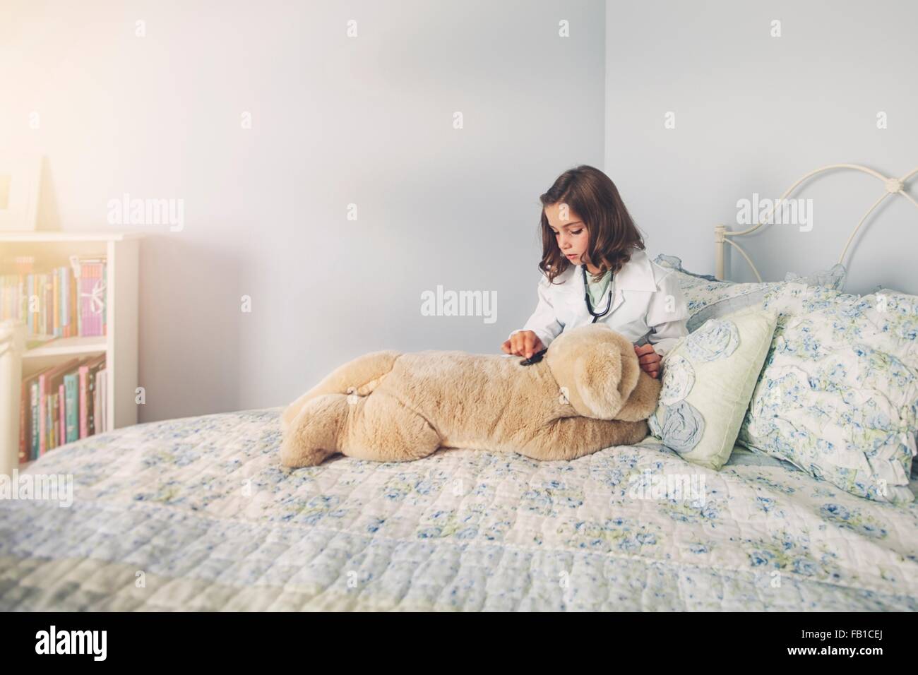 Girl dressed up in lab coat assis au lit en utilisant le stéthoscope soft toy Banque D'Images