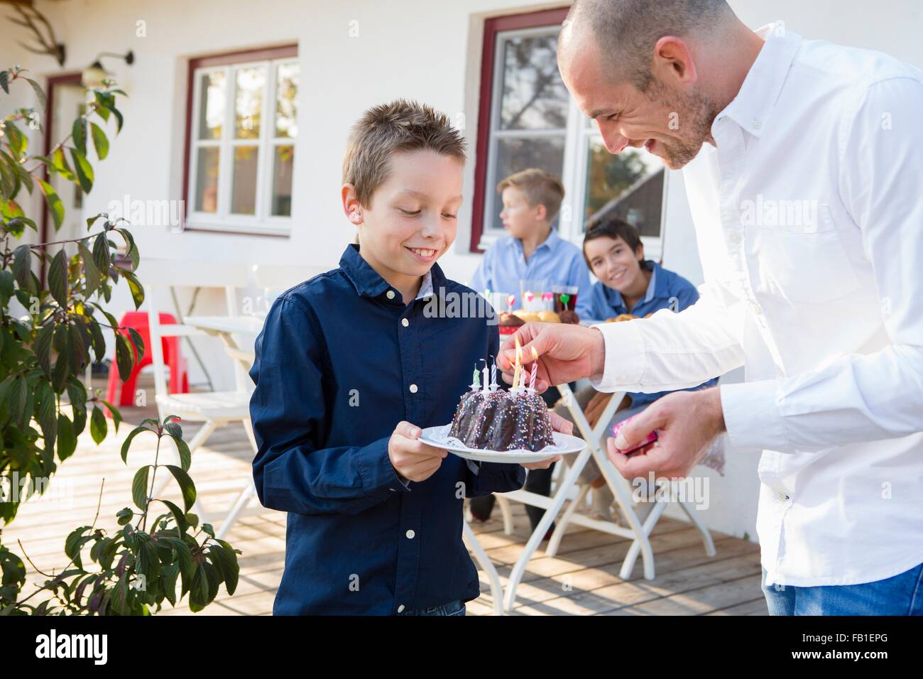 Man fils d'éclairage bougies du gâteau d'anniversaire sur patio Banque D'Images