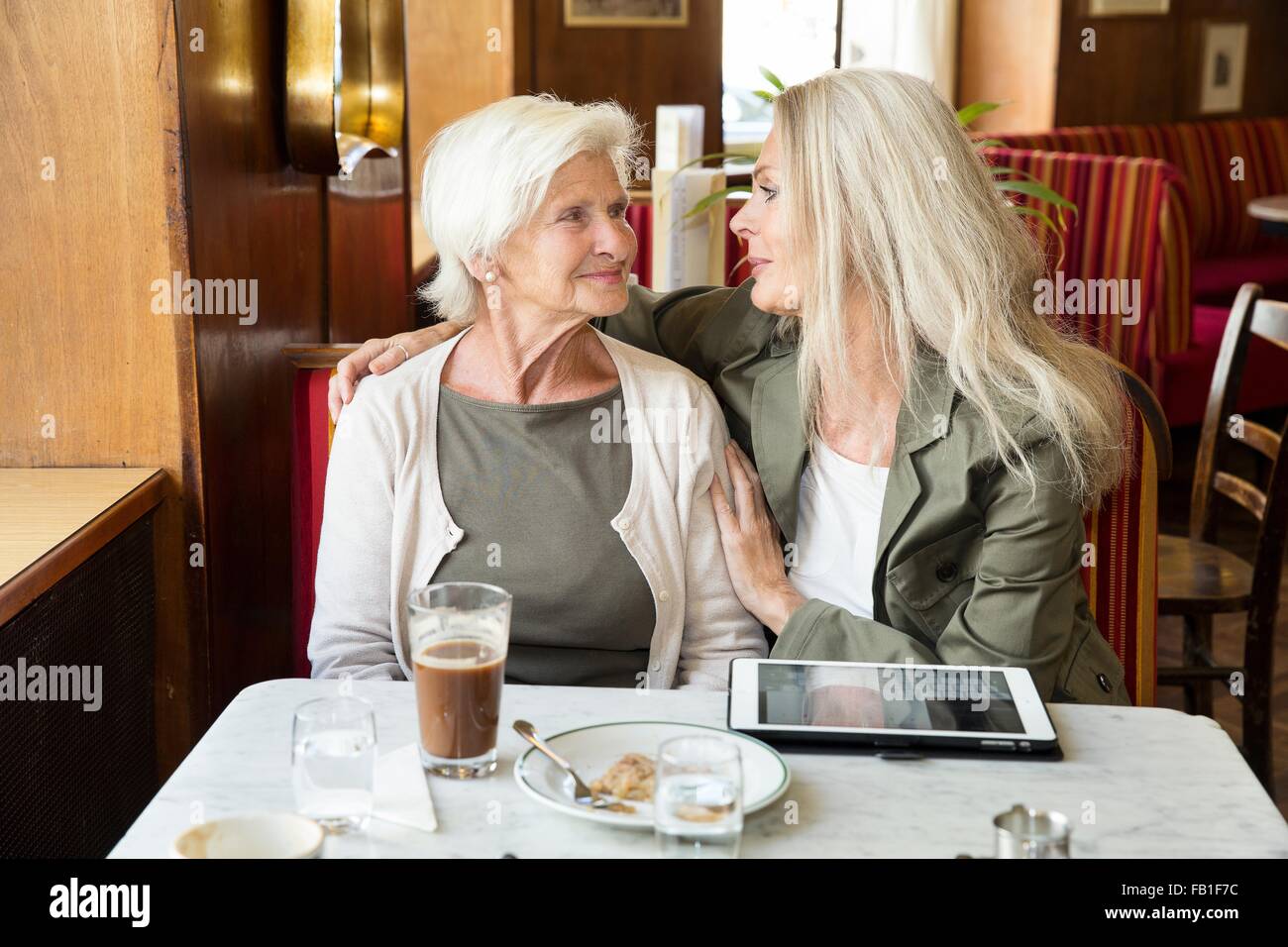 Mère et fille assis ensemble dans un café, une fille bras autour de mère, digital tablet on table Banque D'Images