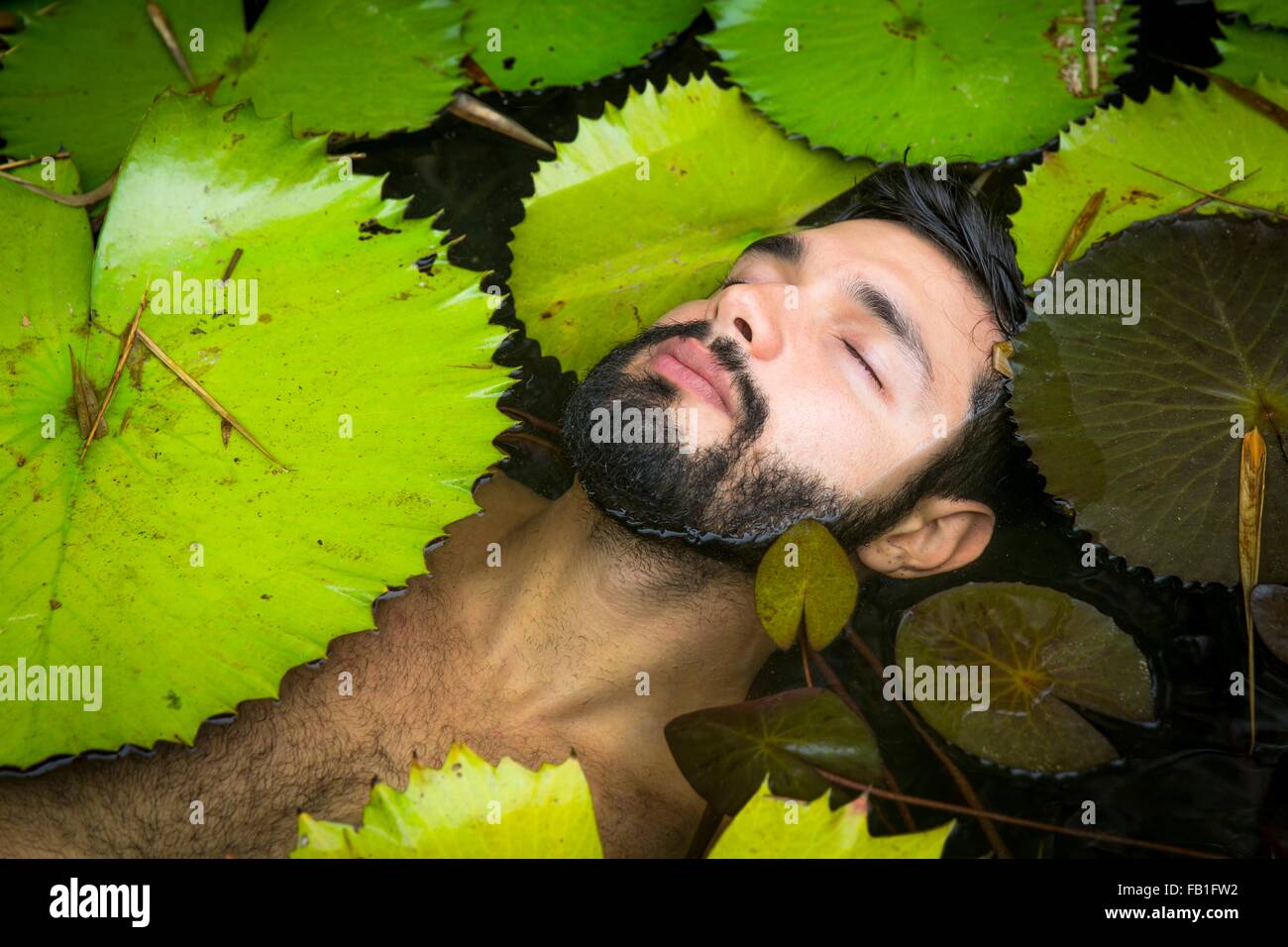 Portrait de jeune homme barbu parmi les nénuphars flottant, les yeux clos, Taiba, Ceara, Brésil Banque D'Images