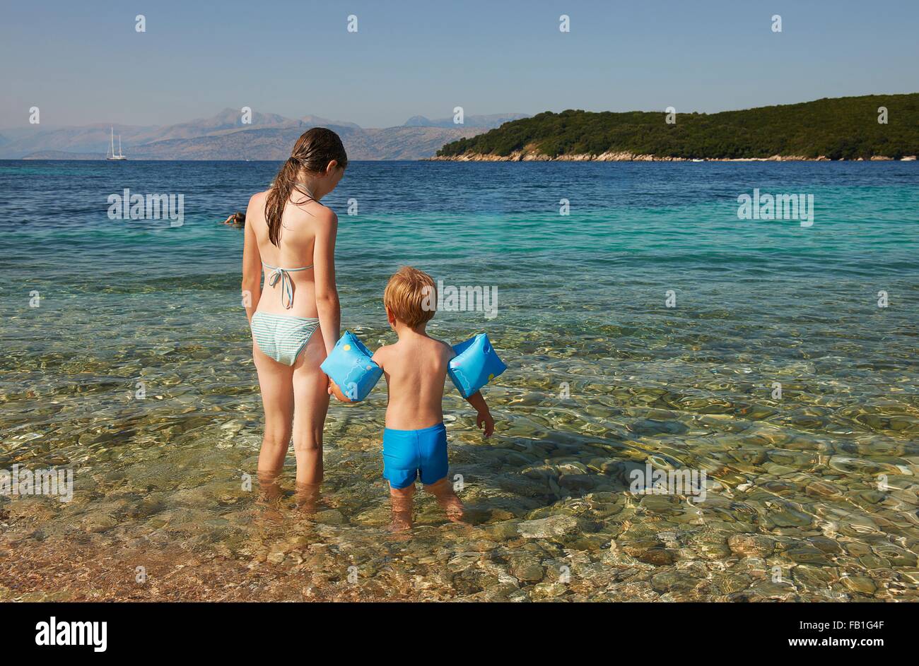 Vue arrière du garçon et fille portant un brassard bleu paddling in sea, Corfou, Grèce Banque D'Images