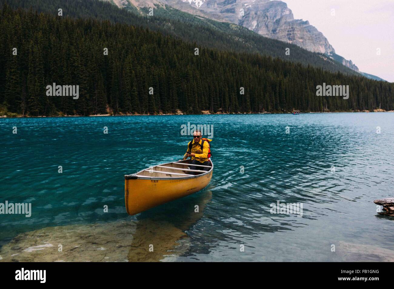 Mid adult man paddling canoe sur le lac Moraine, looking at camera, Banff National Park, Alberta Canada Banque D'Images