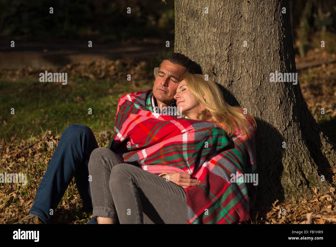 Couple contre tronc de l'arbre enveloppé dans une couverture de nuit Banque D'Images