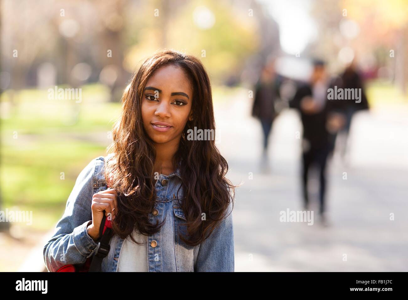 Portrait de jeune femme aux longs cheveux bruns portant veste en jean à la caméra en souriant Banque D'Images