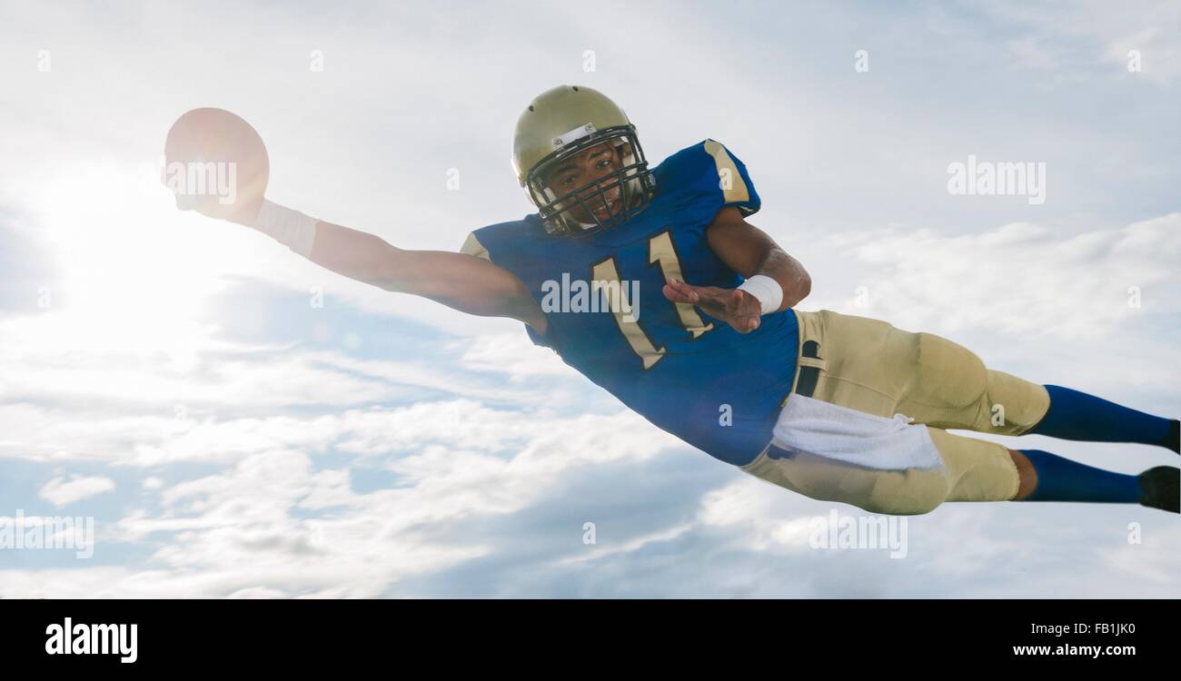 Les adolescents de sexe masculin American football player catching ball mid air contre ciel soleil Banque D'Images