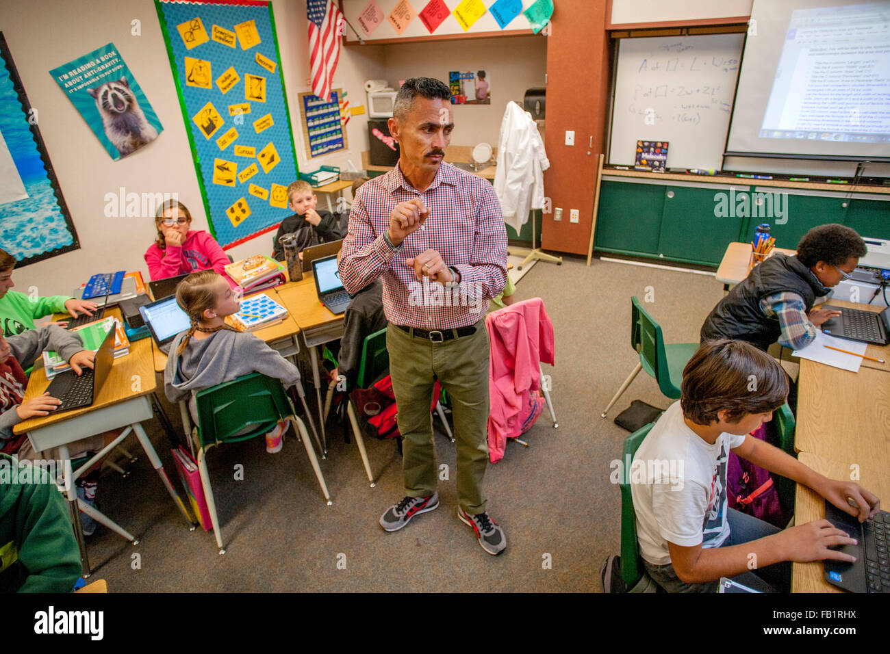 Une cinquième année d'études hispaniques regarde son professeur multiracial students travailler avec des ordinateurs portables dans un San Clemente, CA, école primaire de classe. Banque D'Images