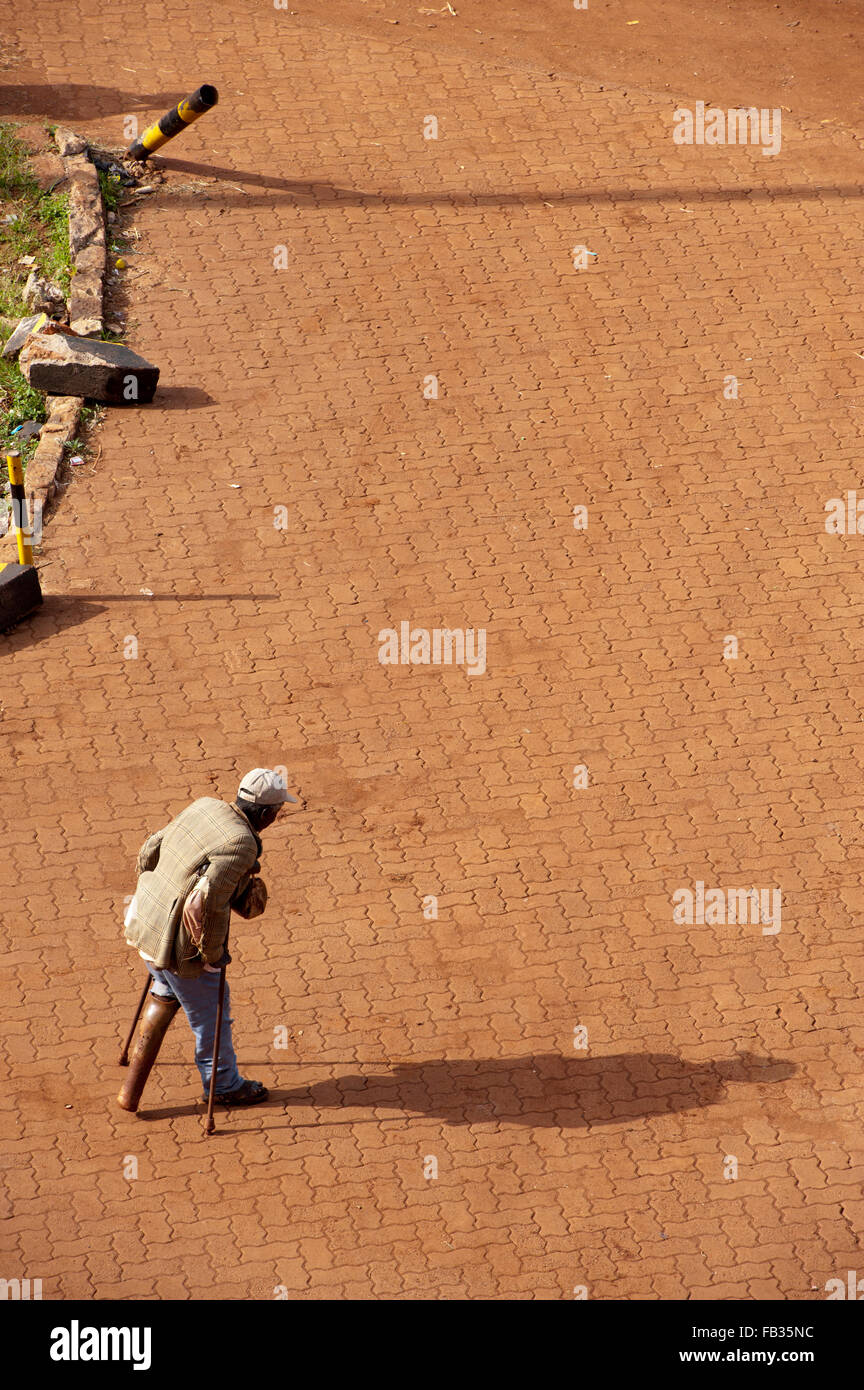 Homme avec une fausse jambe traversant une route pavée, Bulama, au Kenya. Banque D'Images