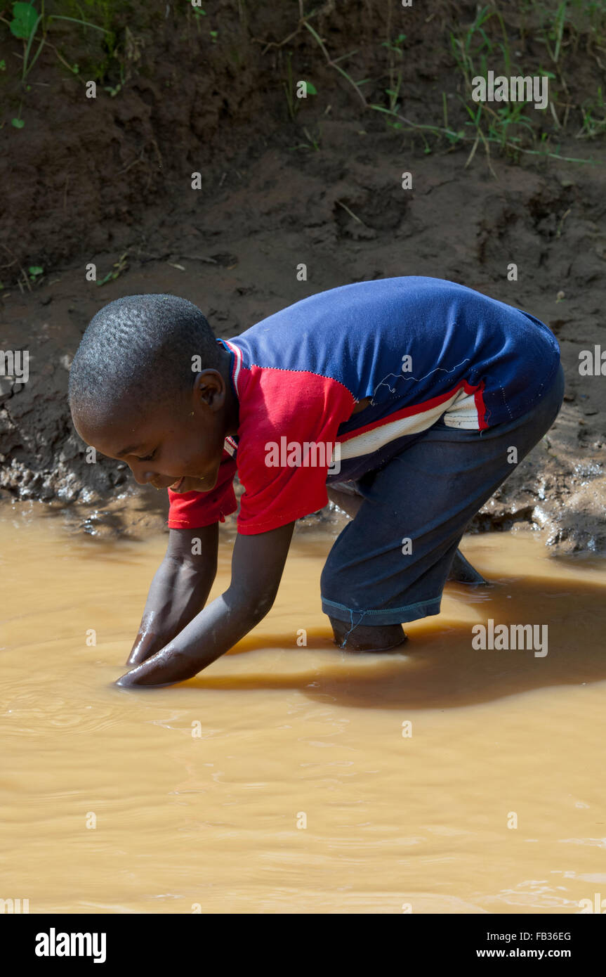 Jeune enfant obtenir de l'eau d'une rivière boueuse, au Kenya. Banque D'Images