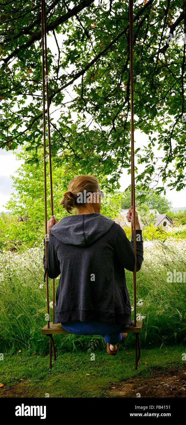 Femme siéger sitting on swing accrocher hanging tree parc parc jardin fleurs d'été fleurs Banque D'Images