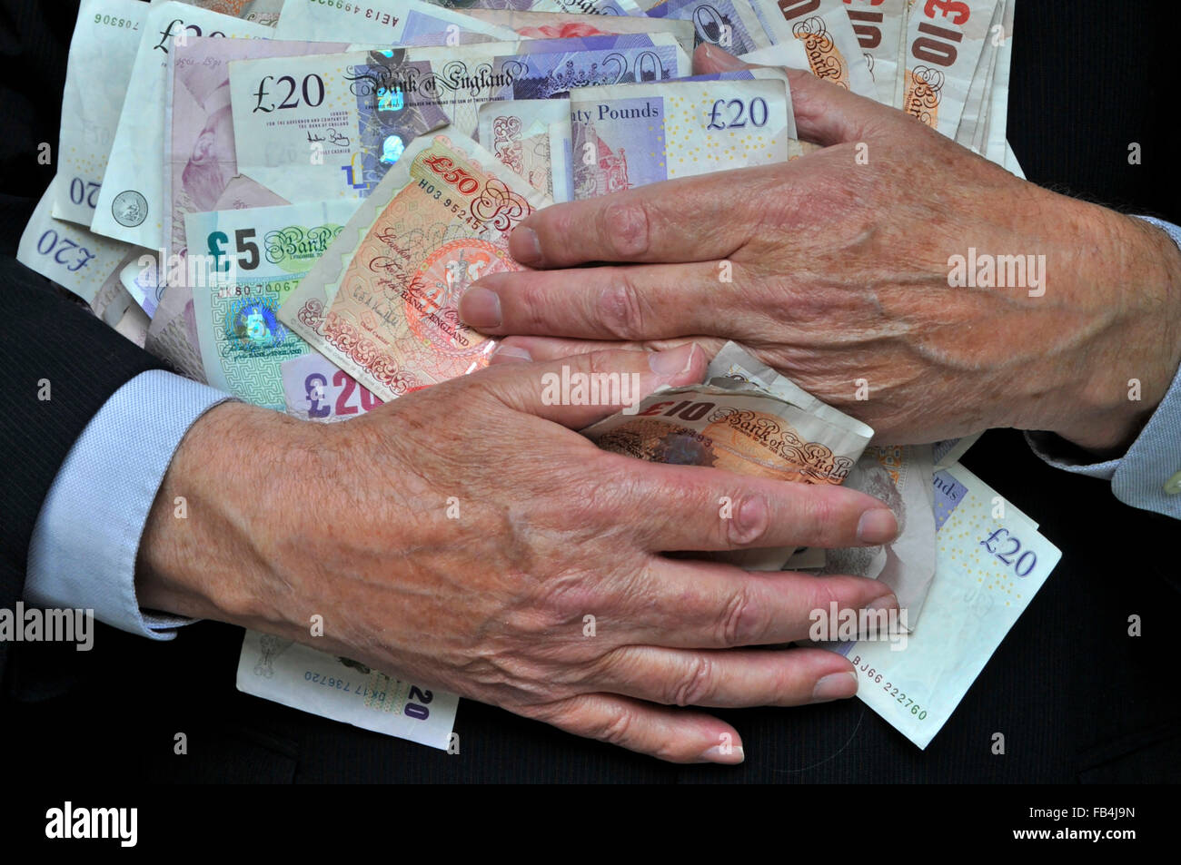 Homme d'affaires en costume mains plus âgées saisissant pile de billets de banque sterling, concept pour des récompenses avides, bonis incitatifs wad d'argent ne le dépensez pas al UK Banque D'Images