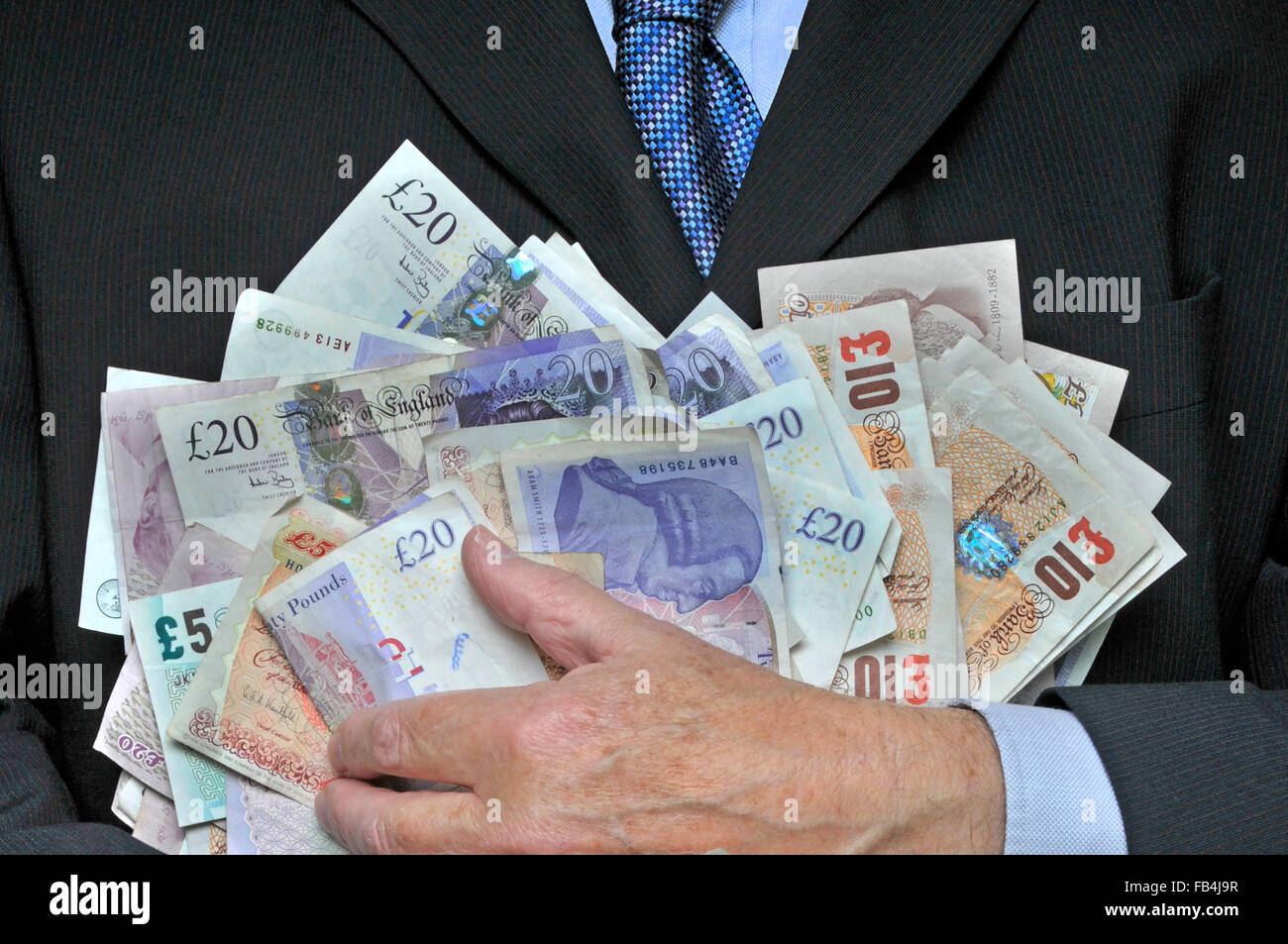 Homme d'affaires en costume et cravate à la main tenant une pile de billets de banque livre sterling image concept pour l'argent dans la main récompense cupidité bonus dépenses d'homme d'affaires Banque D'Images