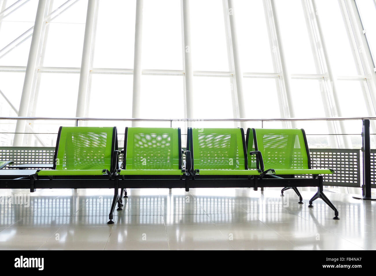 Banc avec sièges vert dans le hall de départ d'un aéroport, avec d'immenses fenêtres en arrière-plan. Banque D'Images